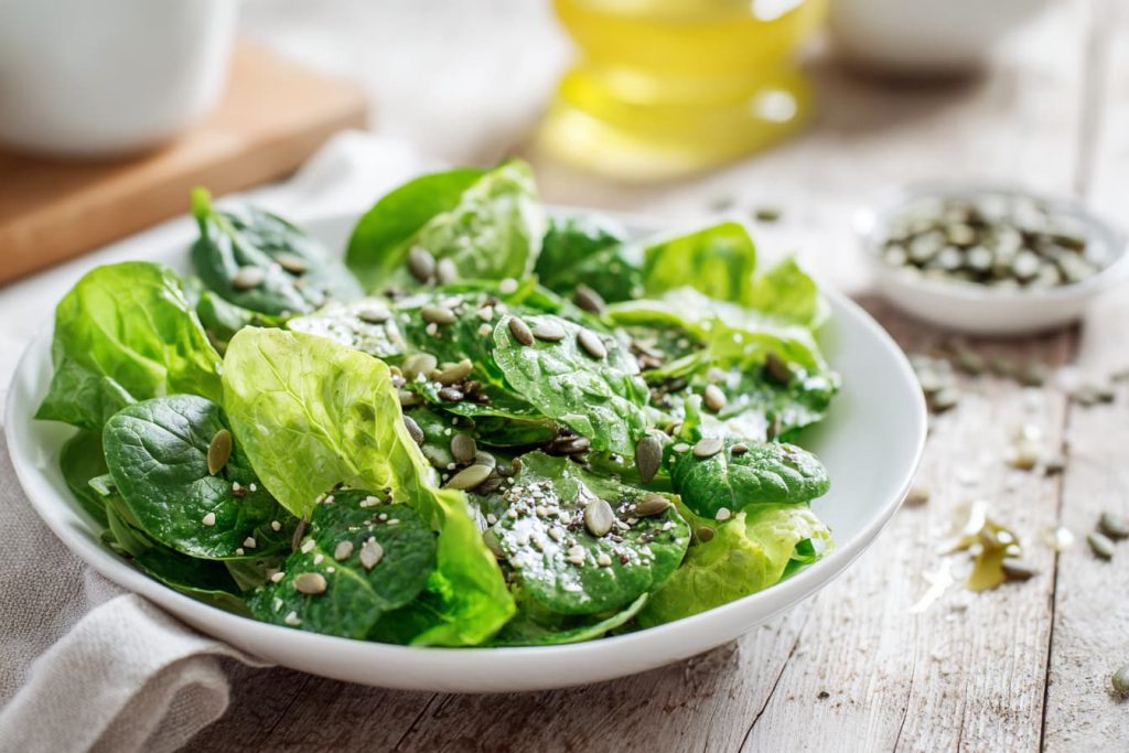 spring greens salad bowl with spinach arugula and herbs, lemon slices and olive oil